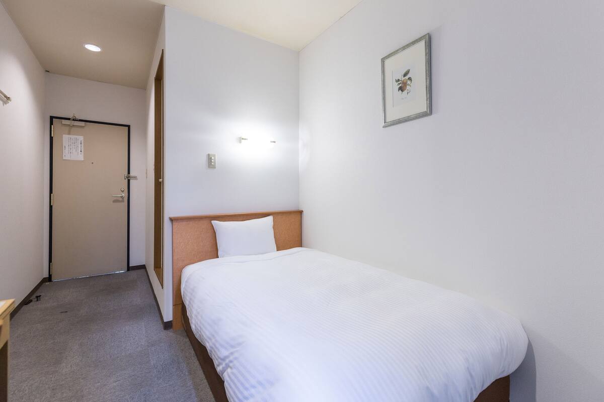 Ein Hotelzimmer mit einem Einzelbett, einem hölzernen Kopfteil, einer weißen Wand und einem gerahmten Bild.