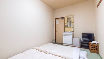 Una habitación pequeña y limpia con cama, lavamanos, espejo, televisor y una mesita.