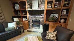 Un salon doté d’une cheminée, de canapés en cuir, d’un pouf vert et d’un manteau de cheminée en pierre.