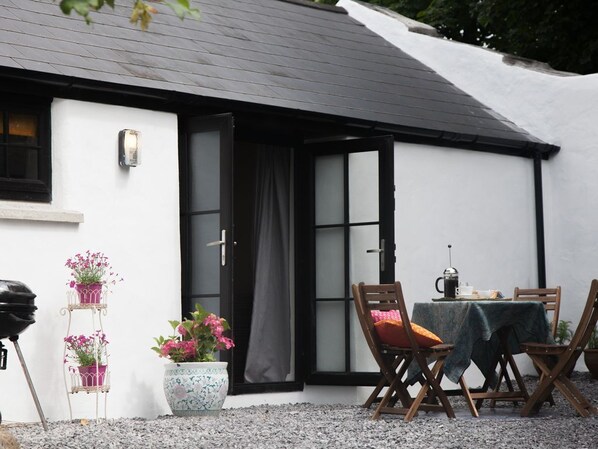 A white building with a black roof, a door, and a table with chairs outside.