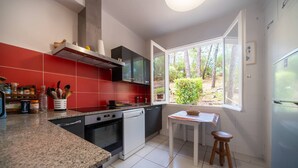 A modern kitchen with red and black cabinetry, a built-in oven, a dishwasher, and a window with a view of trees. - Villa LE MENEZ for 10 persons with view on the marine lake (SOORTS HOSSEGOR)