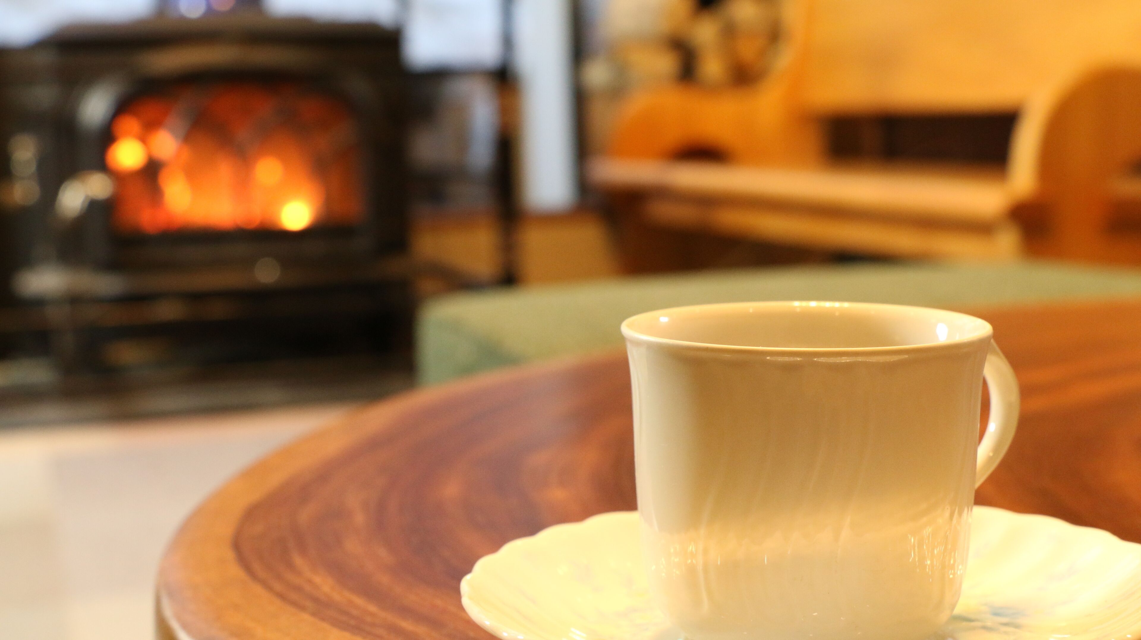 Una taza blanca sobre un plato, una mesa de madera y un fondo borroso con una chimenea.