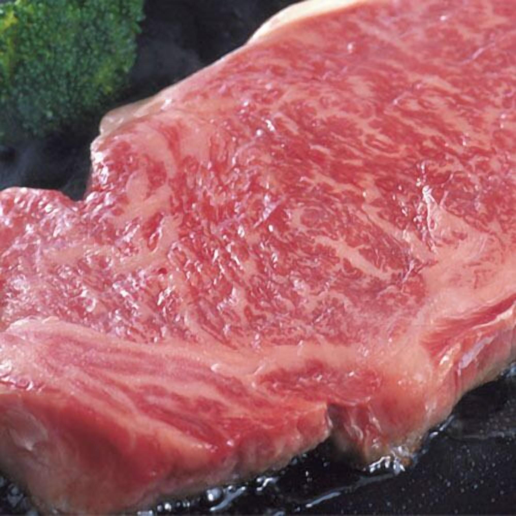 A raw steak on a grill with a broccoli side.