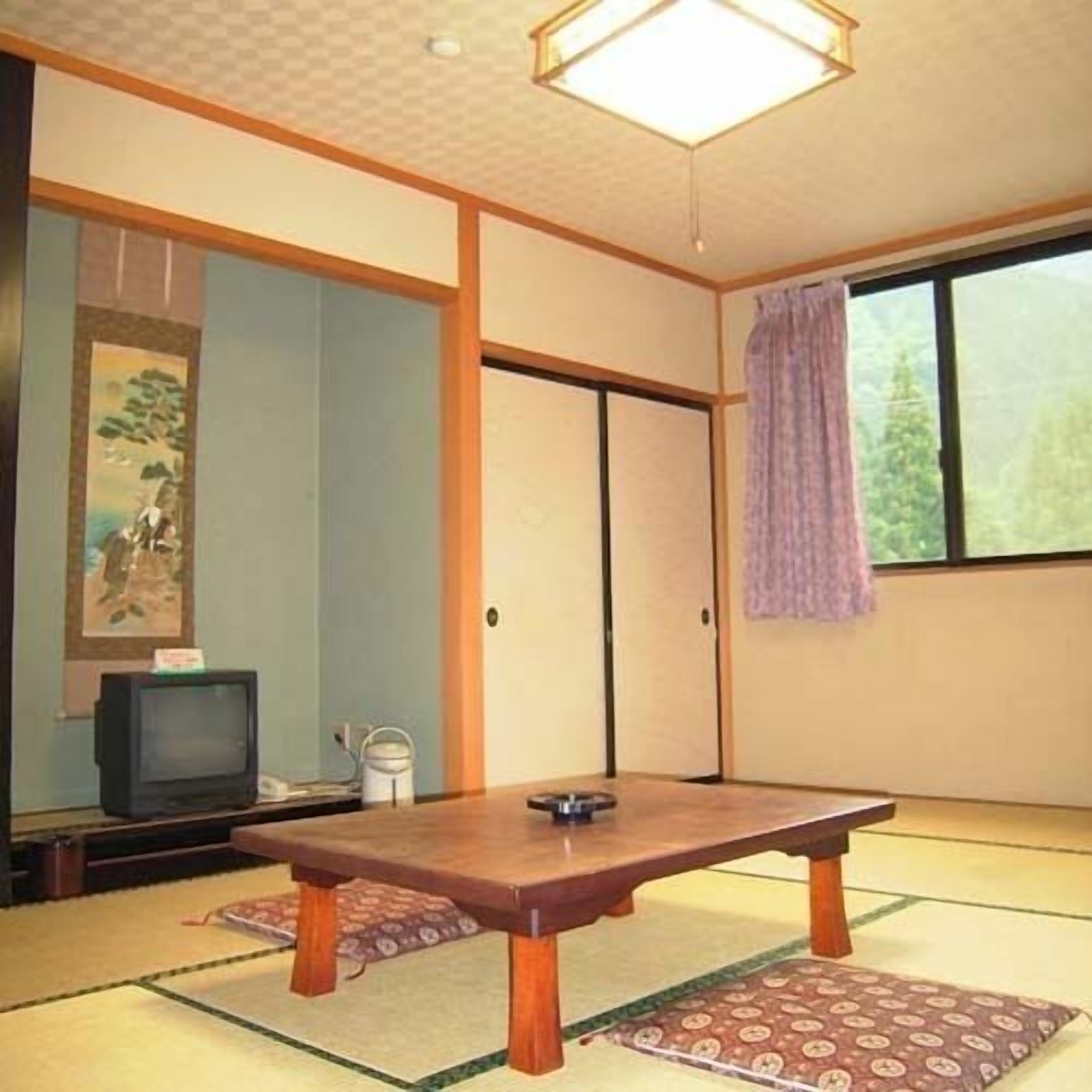 A traditional Japanese room with tatami flooring, a low table, a television, and a sliding door.