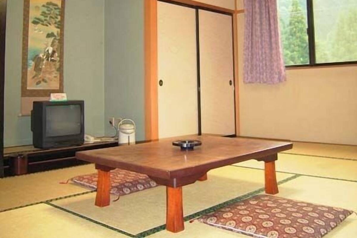 Una habitación japonesa tradicional con suelo de tatami, una mesa baja, un televisor y una puerta corredera.