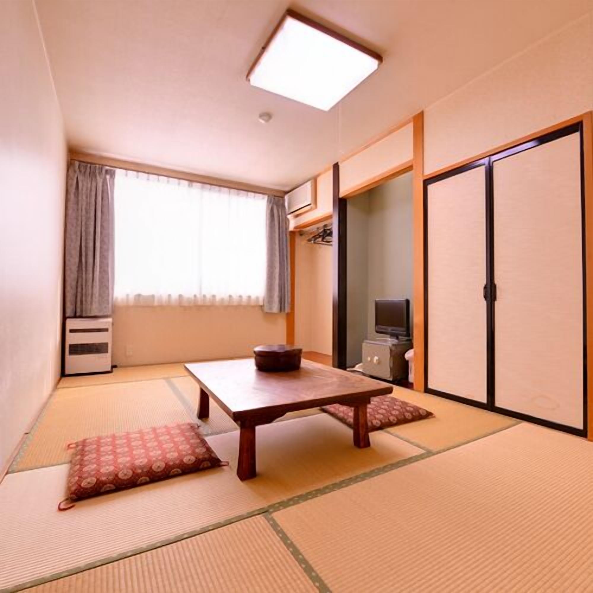 A traditional Japanese room with tatami flooring, a low table, a television, and sliding doors.