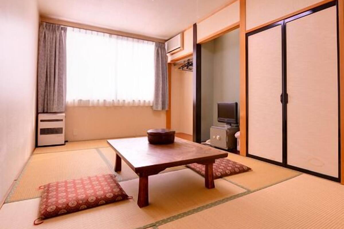 Una habitación tradicional japonesa con suelo de tatami, una mesa baja, un televisor y puertas correderas.