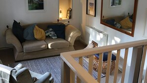 Un salón con sofá, una silla, una mesita y un espejo. Hay cuadros enmarcados en la pared y una ventana con vistas al exterior.