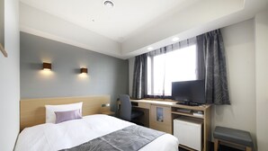Ein Hotelzimmer mit einem Bett, einem Schreibtisch mit Fernseher, einem Sessel und einem kleinen Schrank.