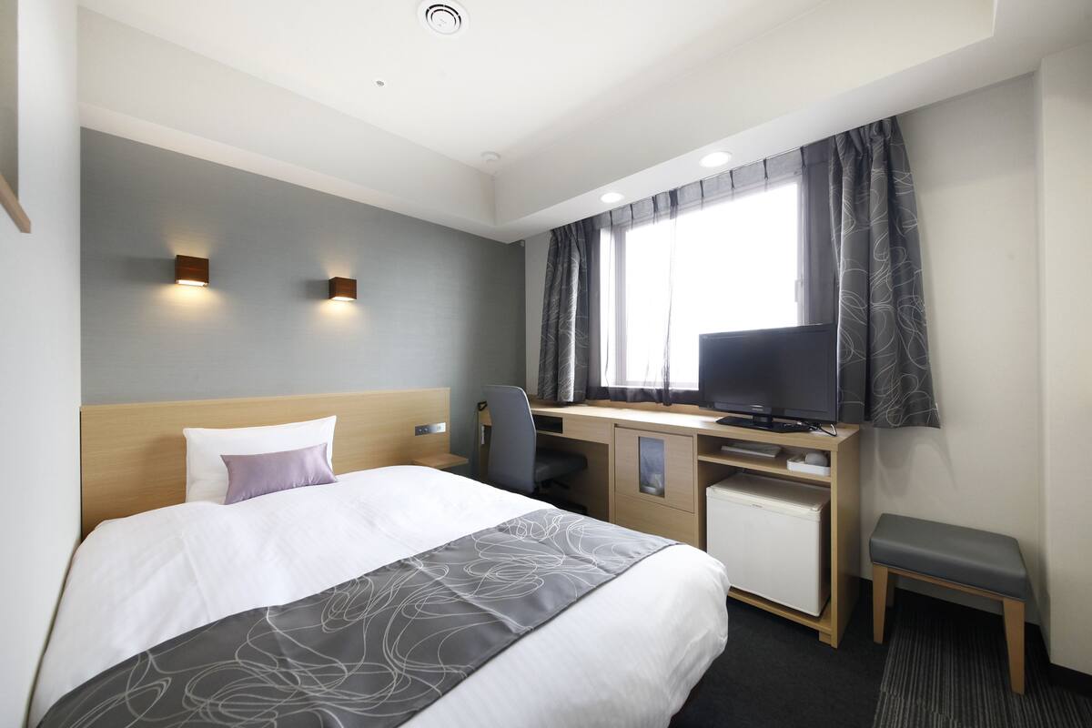 Ein Hotelzimmer mit einem Bett, einem Schreibtisch mit Fernseher, einem Sessel und einem kleinen Schrank.