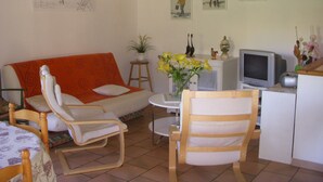 Un salón con sofá, dos sillones, una mesita con un jarrón de flores, televisor y cuadros en las paredes.
