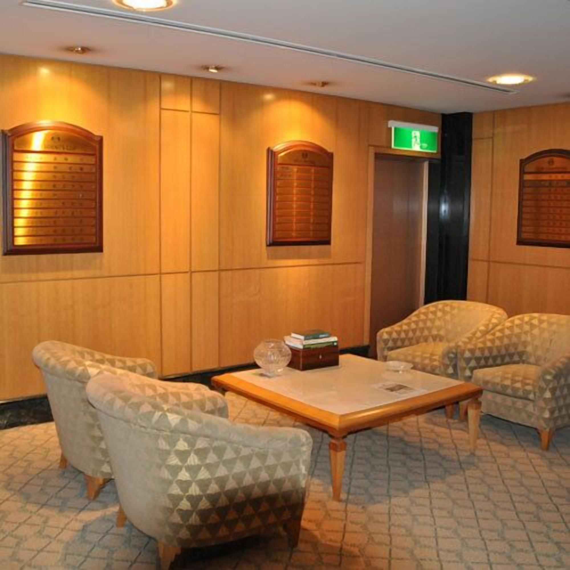Un vestíbulo con sillones estampados, un mostrador de recepción de madera y un ascensor.