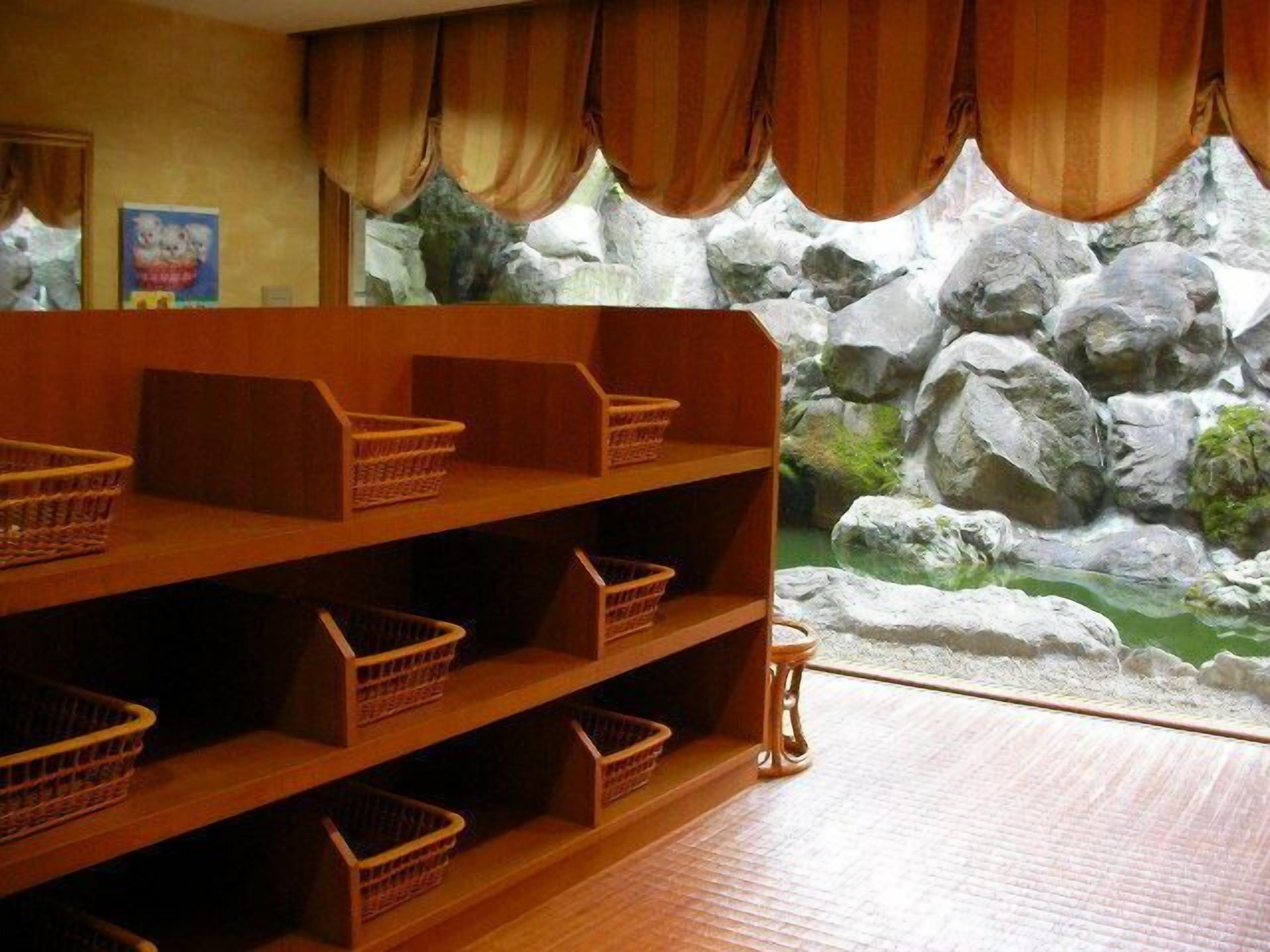 A room with wooden shelves and baskets, a stone wall with a rock garden view, and a small table.
