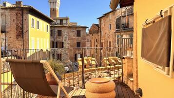 A balcony with a chair and ottoman, overlooking a courtyard with buildings and a tower.