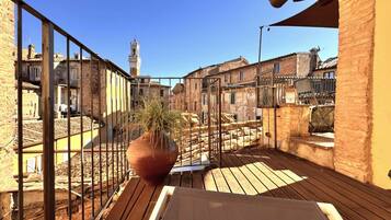 Una terrazza sul tetto con vista su edifici storici e una torre, con un vaso di terracotta grande e una ringhiera in metallo.
