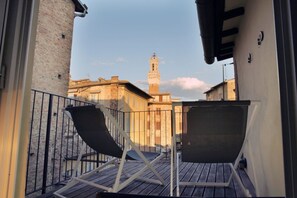 A balcony with two lounge chairs and a view of a historic building with a tower.