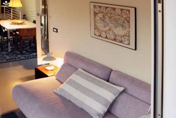 A room with a purple sofa, a striped pillow, a table with chairs, and a wall-mounted map.