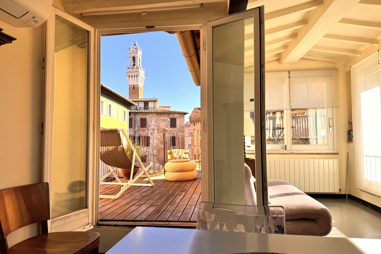Une chambre avec vue sur un bâtiment historique et une tour, une terrasse en bois à l’extérieur et une porte vitrée donnant sur un balcon.