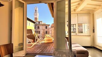Une chambre avec vue sur un bâtiment historique et une tour, une terrasse en bois à l’extérieur et une porte vitrée donnant sur un balcon.