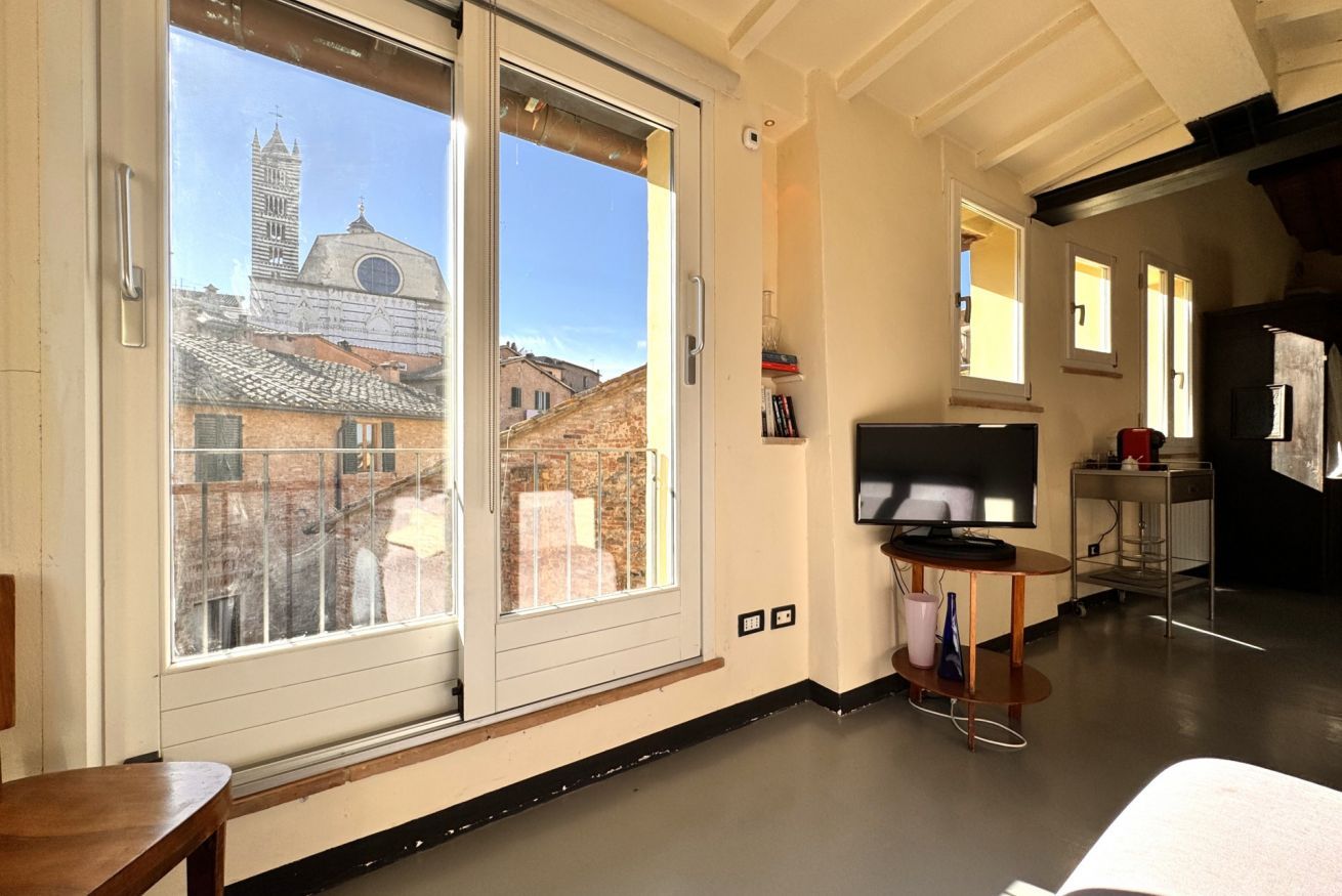 A room with a large window, a flat-screen TV, and a wooden bench.