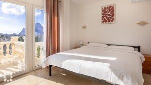 A hotel room with a bed, a balcony with curtains, a city view, and a mountain in the background. - Villa RICA by Abahana Villas (Calpe)