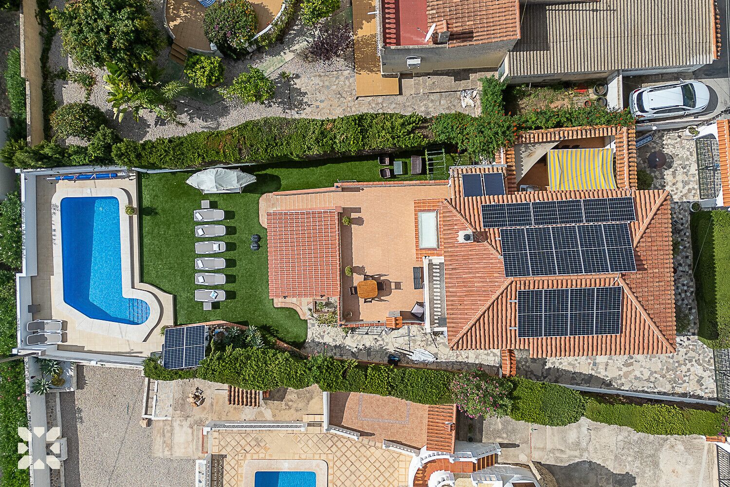Luchtbeeld van een woonhuis met een zwembad, meerdere buitenzitplaatsen en zonnepanelen.