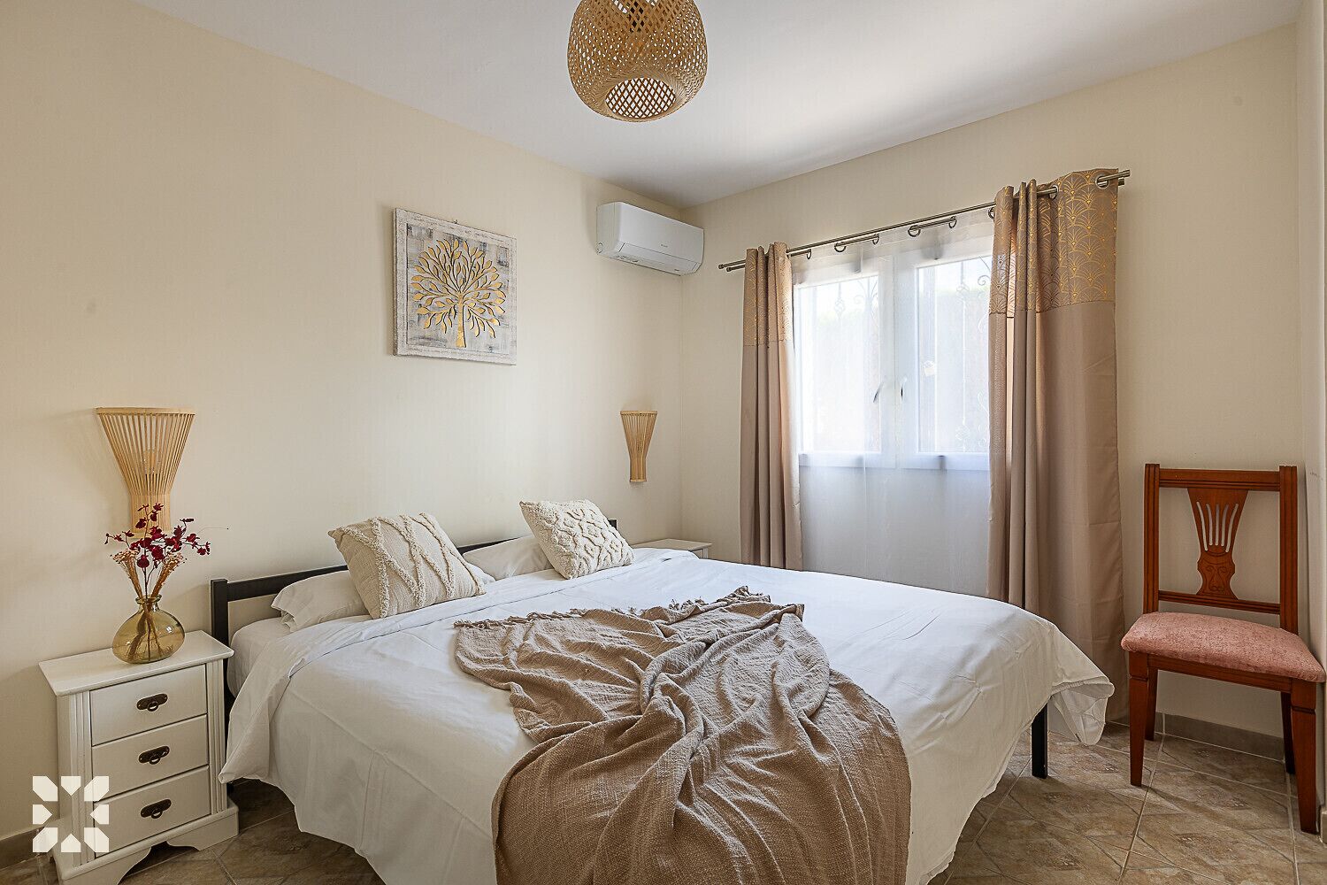 A bedroom with a bed, bedside tables, a chair, a window with curtains, and wall art.