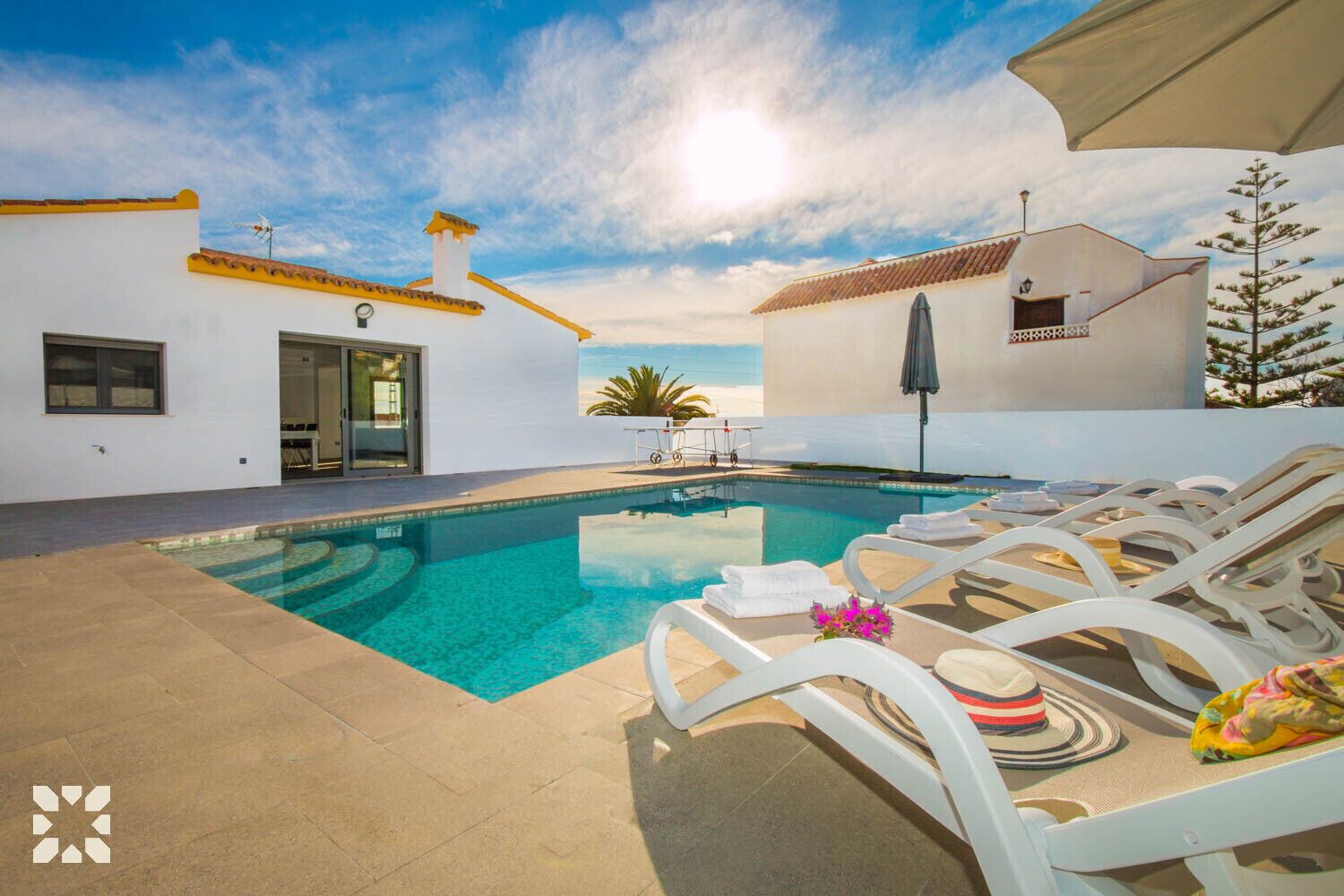 A swimming pool with lounge chairs, a door, and a view of the ocean.
