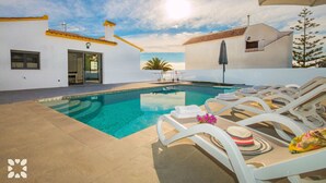 A swimming pool with lounge chairs, a door, and a view of the ocean.