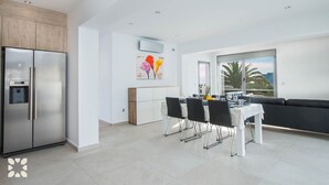 A modern kitchen with a built-in refrigerator, a dining area with a table and chairs, and a large window offering a view of palm trees.