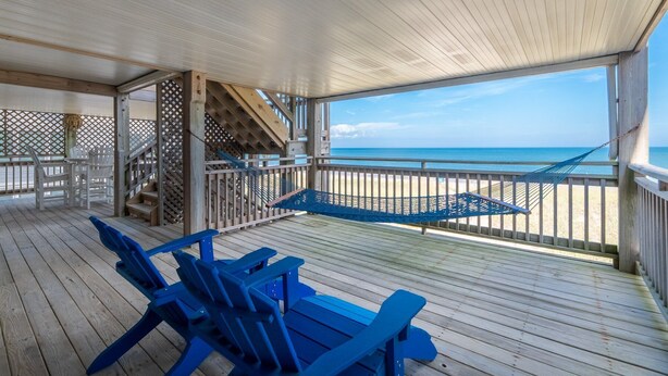 A covered deck with blue Adirondack chairs, a hammock, and a view of the beach.