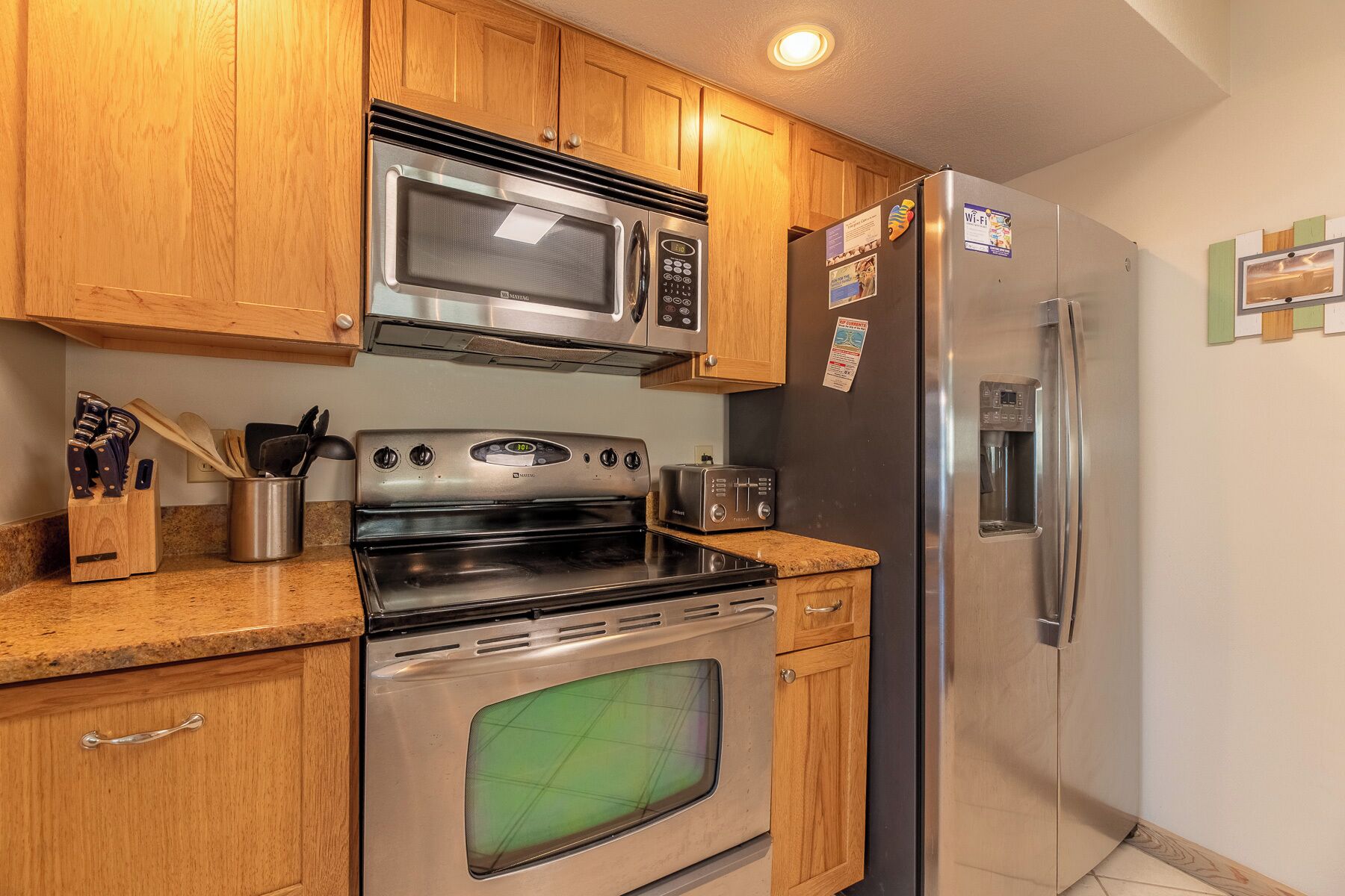 A kitchen with wooden cabinets, a stainless steel microwave, oven, and refrigerator, a toaster, and a knife block.