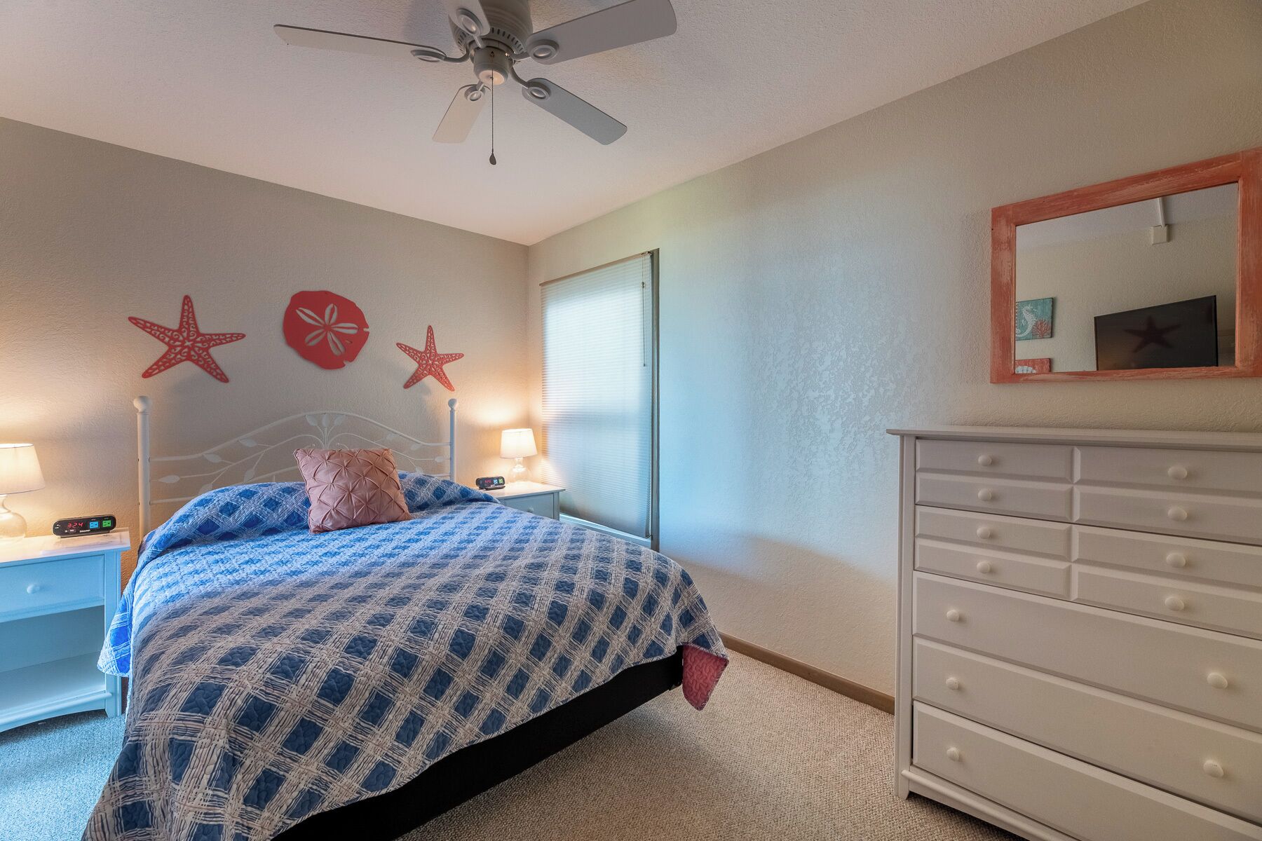 A bedroom with a bed, bedside tables, a dresser, a ceiling fan, and decorative starfish on the wall.