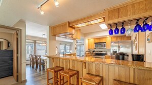 A kitchen with wooden cabinets, a stainless steel refrigerator, and a bar area with stools.