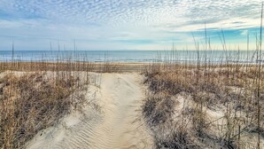 A sandy beach path with sparse vegetation leading to the ocean.
