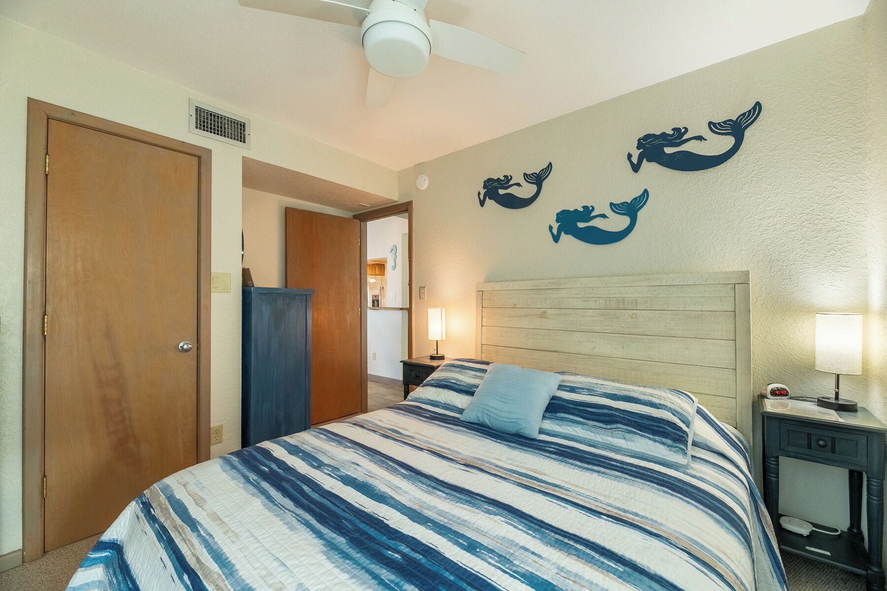 A hotel room with a bed, a nightstand, a lamp, and a wall with mermaid decorations.
