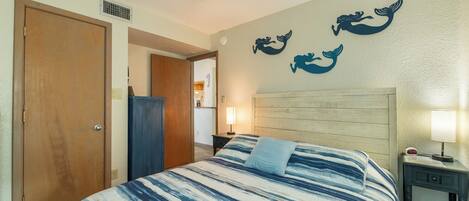 A hotel room with a bed, a nightstand, a lamp, and a wall with mermaid decorations.