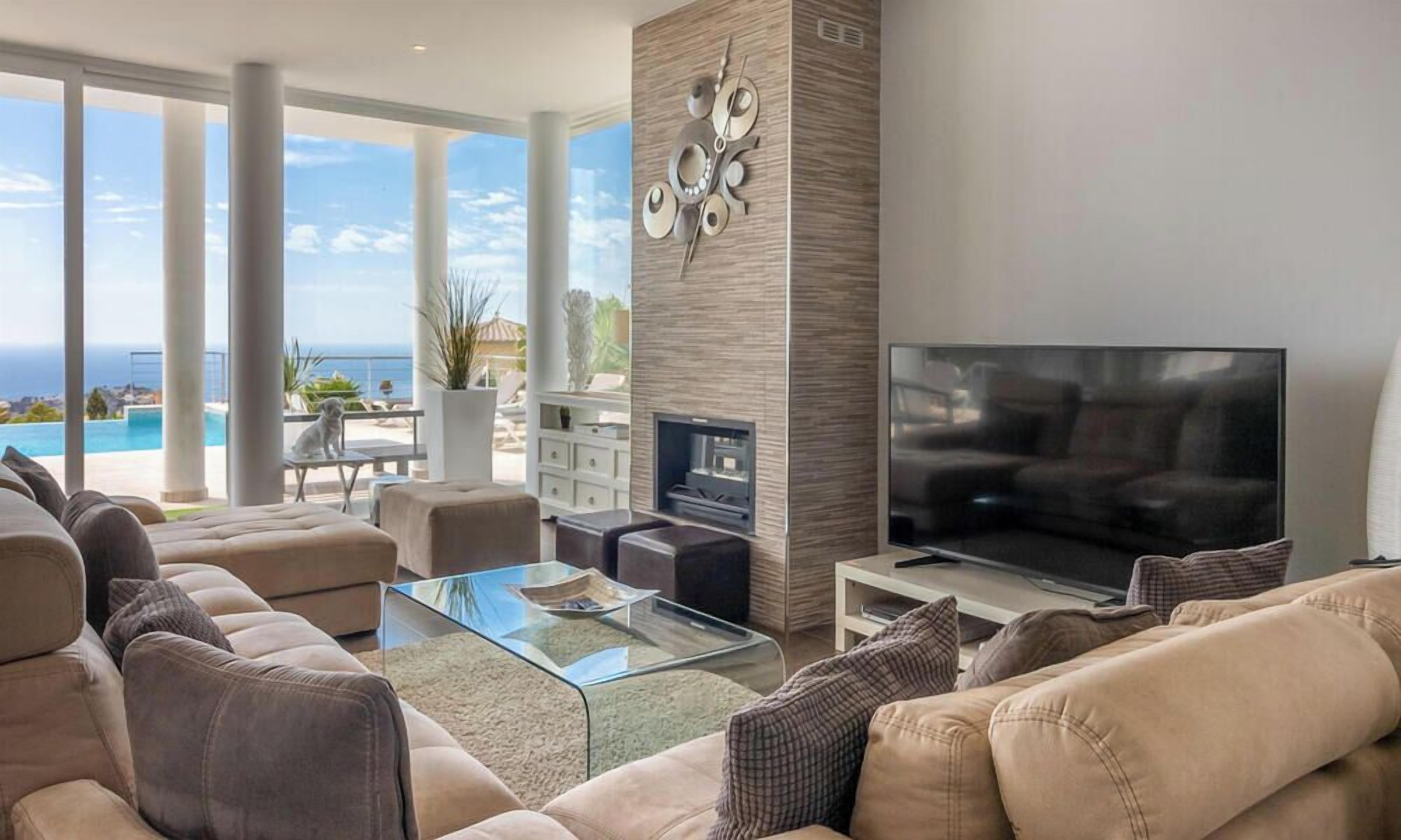 Uma sala de estar moderna com uma televisão grande, assentos confortáveis, lareira e vista para o oceano.