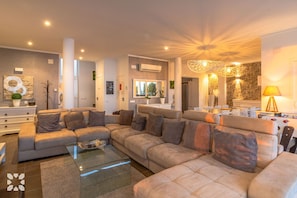 A modern living room with a sectional sofa, a glass coffee table, and a dining area with chairs.