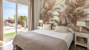 A bedroom with a large bed, two bedside tables with lamps, a view of the outdoors, and a tropical leaf mural on the wall. - Villa PUNTA VISTA by Abahana Villas (Benitachell)