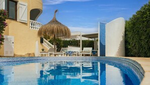 Piscina com espreguiçadeiras e um guarda-sol de palha.