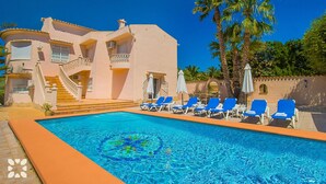 A hotel with a swimming pool, blue lounge chairs, and palm trees. - Villa LUNA FELIZ by Abahana Villas (Calpe)