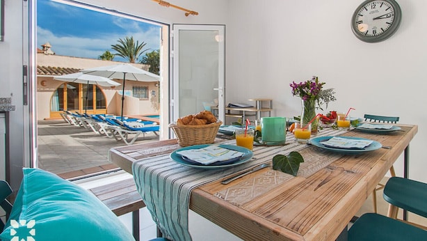 A dining area with a wooden table set for breakfast, a wicker basket, and a clock on the wall. - Villa LUNA FELIZ by Abahana Villas (Calpe)