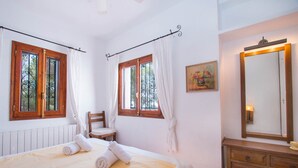 A bedroom with a bed, a chair, a dresser, and two windows with curtains.