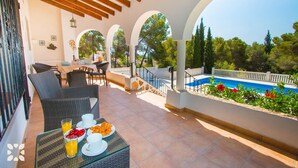 A covered outdoor area with a pool, dining setup, and a view of trees.