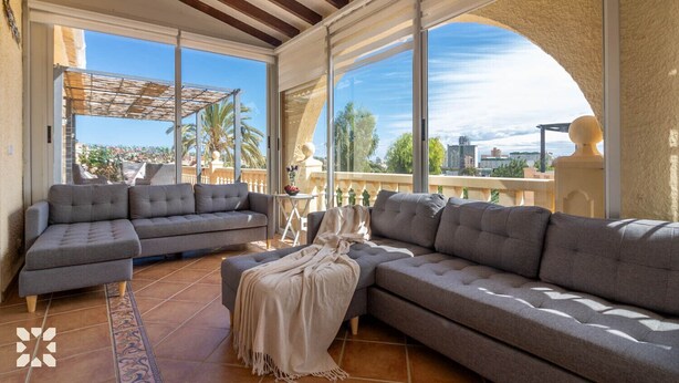 Een zonnig terras met een grijze modulaire bank, een bijzettafeltje en een decoratieve parasol.