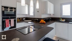 Een moderne keuken met witte kasten, een zwart aanrecht, een inbouwoven, een spoelbak en hangende lampen.
