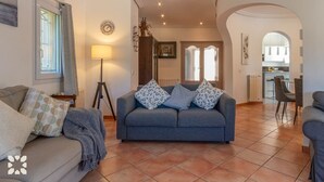 Een woonkamer met een grijze bank, een vloerlamp en een eethoek met stoelen en een tafel.