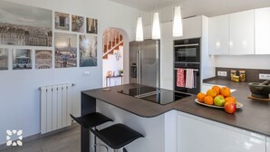 Een moderne keuken met witte kasten, een roestvrijstalen koelkast, een inbouwoven en een fruitschaal op het aanrecht.