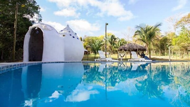A pool with a white dome-shaped structure and a thatched-roof hut. - Pousada Chapada dos Veadeiros (Alto Paraíso de Goiás)